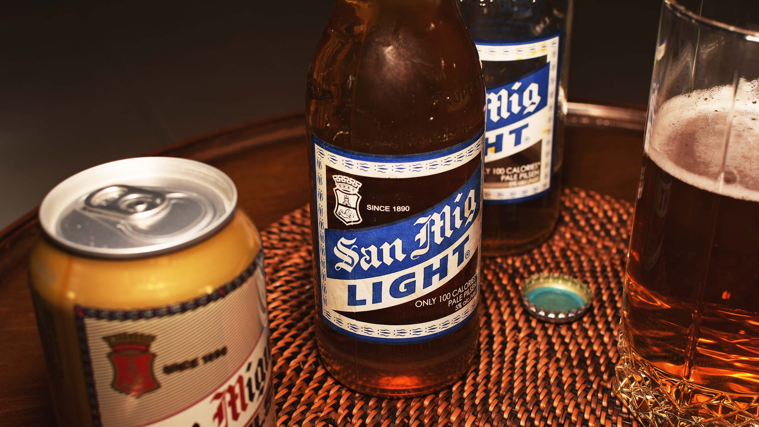A styled photo of bottles of San Miguel Light, a can of Pale Pilsen, and a glass of beer