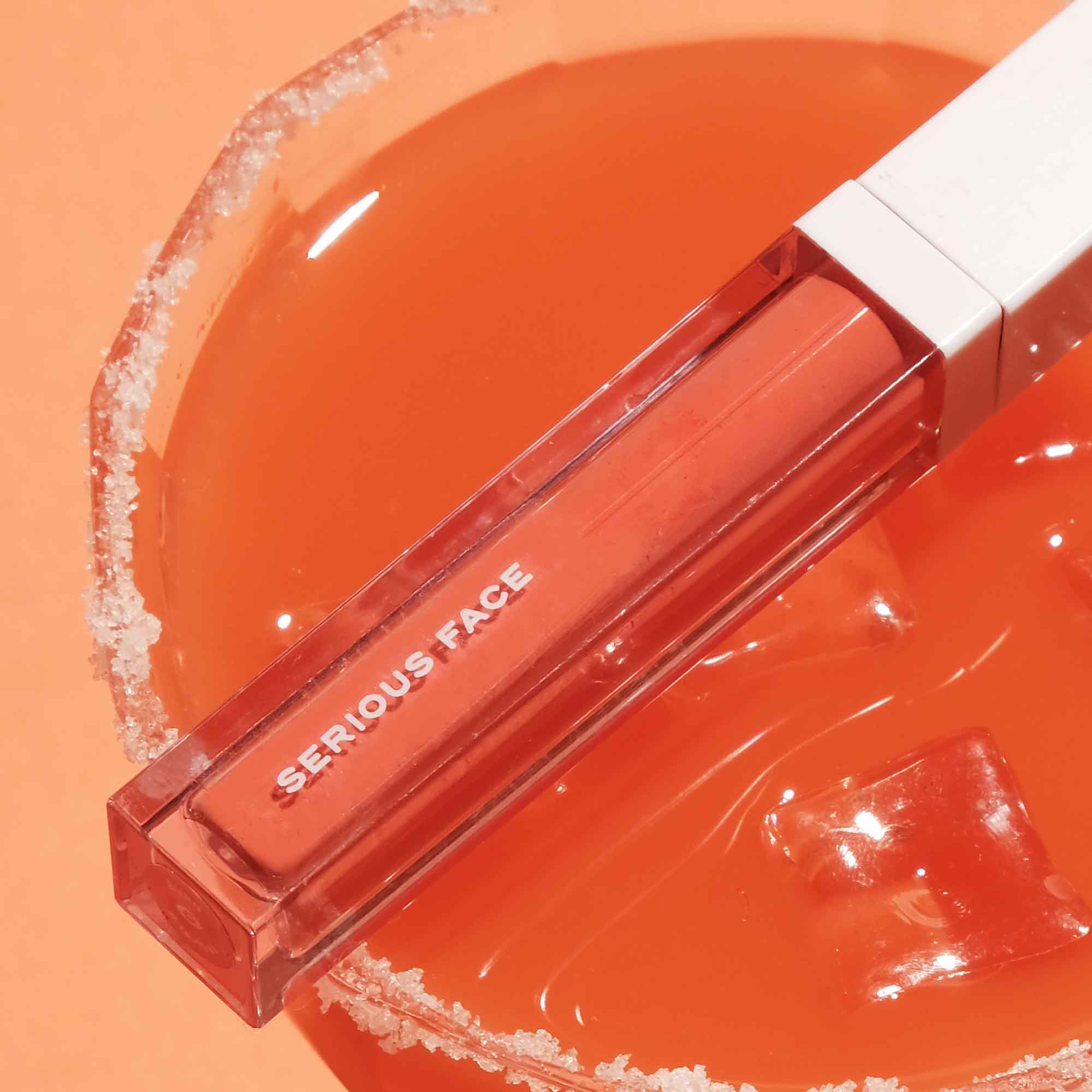A photo of Serious Face's orange lipstick or beauty stick on a cocktail glass