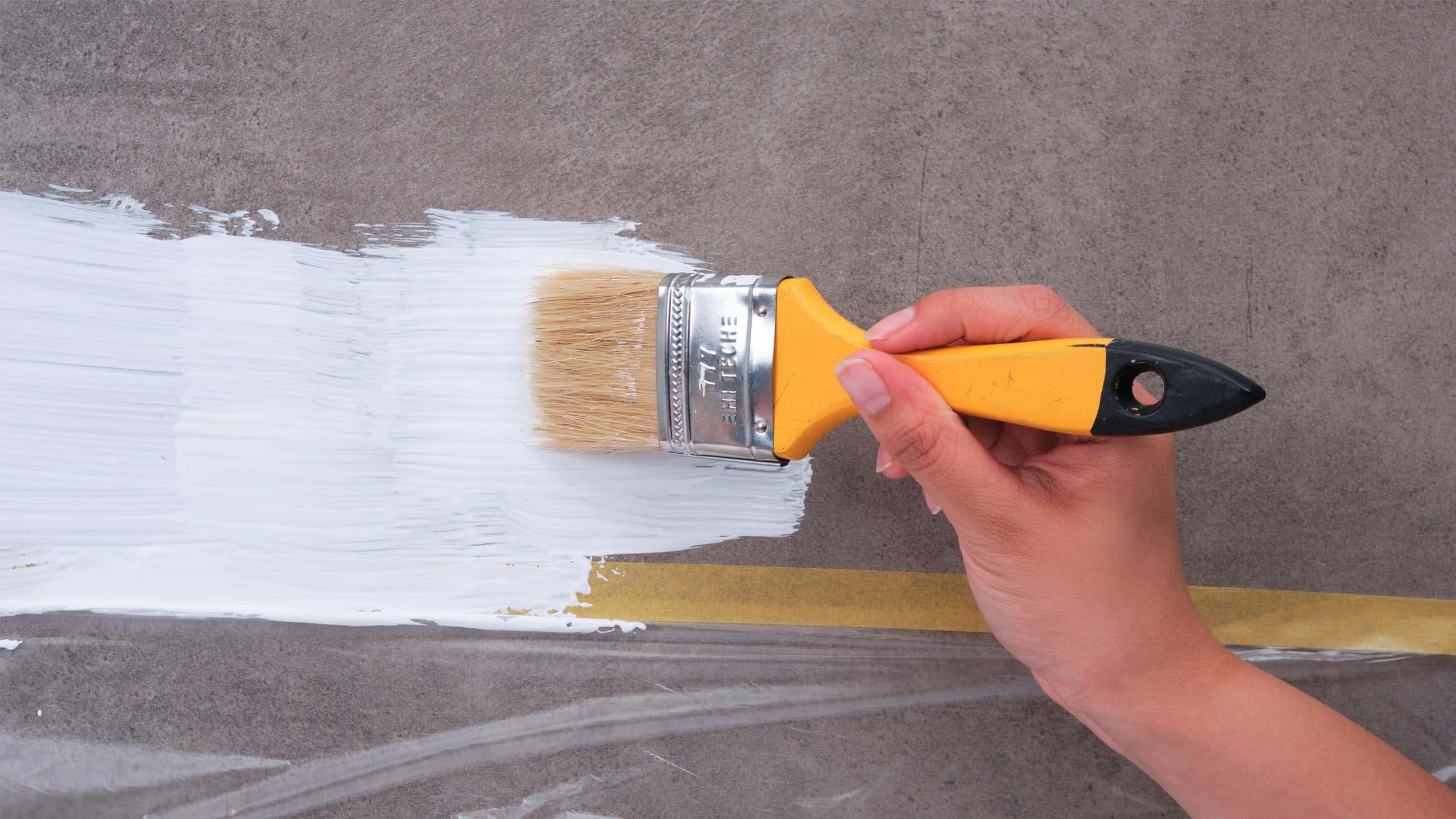 A hand painting the wall white with a paintbrush